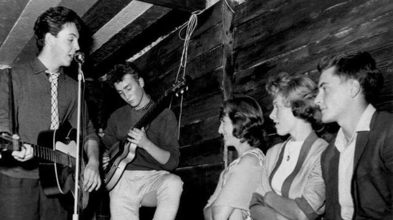 Vintage black-and-white photograph cropped to show three people watching Paul McCartney and John Lennon perform a song.