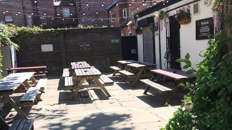 The outdoor patio of Ye Cracke pub with several wooden picnic tables.