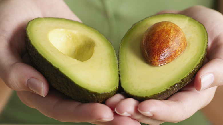 hands holding sliced avocado