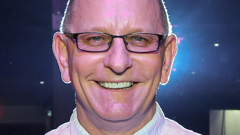 Chef Robert Irvine smiling with arms out, in a busy restaurant.