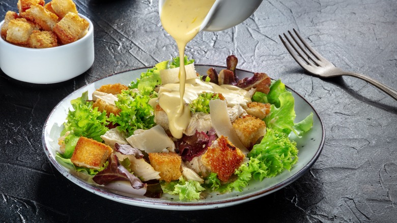 pouring caesar dressing on salad