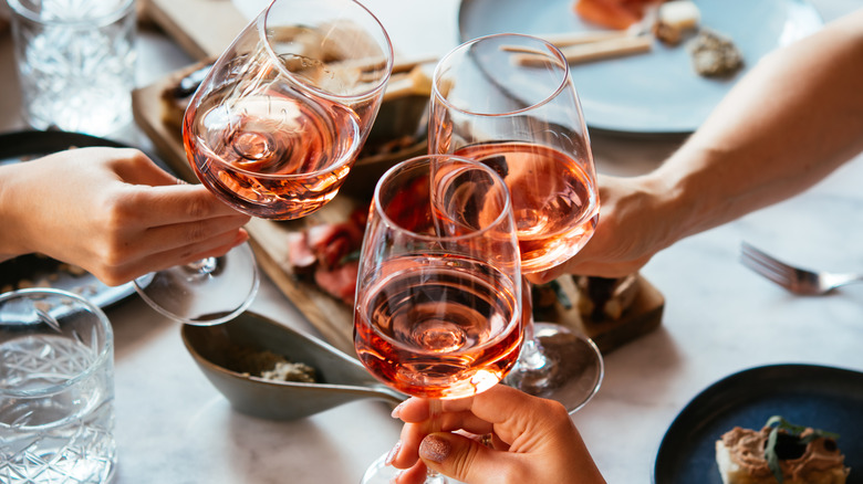 People toasting across a table with three glasses of rose wine