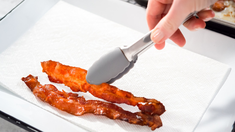 Bacon being placed on paper towel to absorb grease
