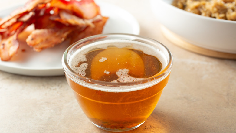 glass bowl of bacon grease with bacon in the background