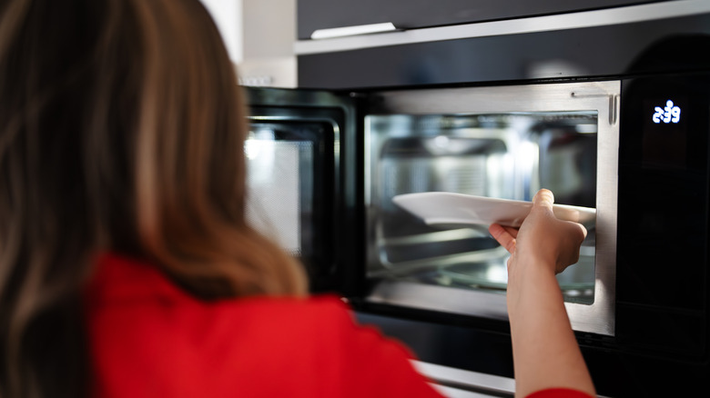 woman putting a plate in microwave to reheat food