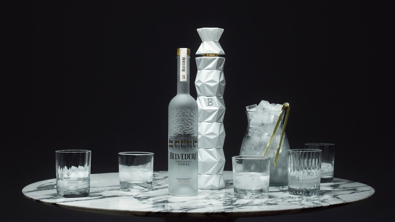 A bottle of Belvedere vodka surrounded by rocks glasses on a marble table