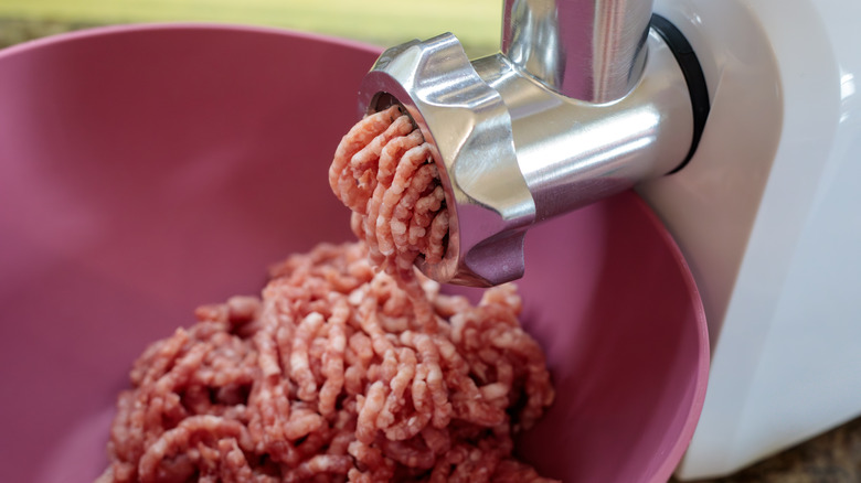 A meat grinder grinding beef into a pink bowl