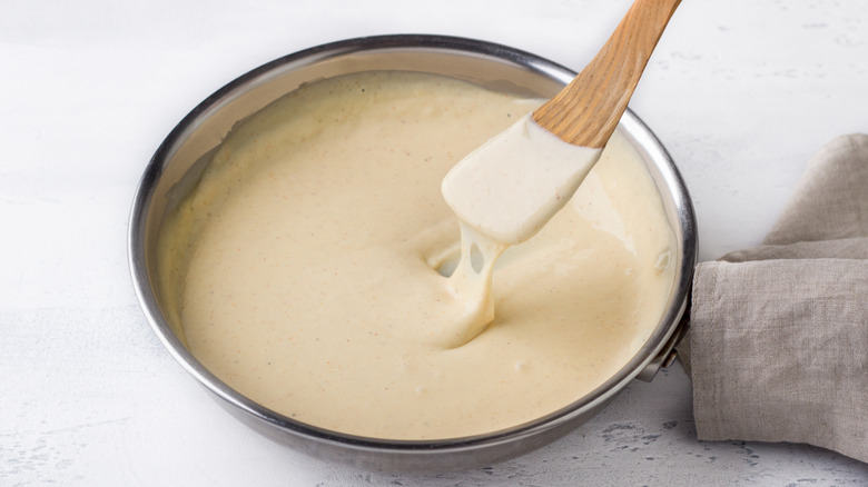 Cheese sauce in a stainless steel bowl being scooped up with a wooden spoon
