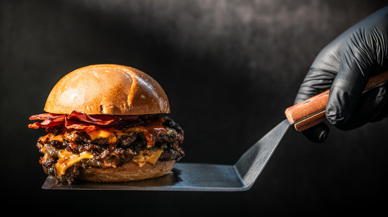 A gourmet cheeseburger with bacon on a spatula