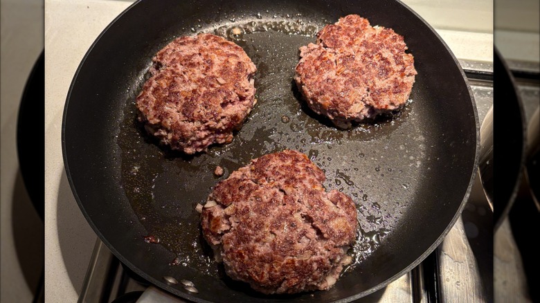 Three burgers frying in a pan close to the sides