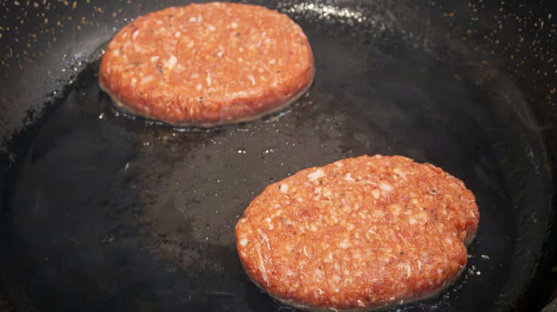 Two burger patties cooking in a pan far apart