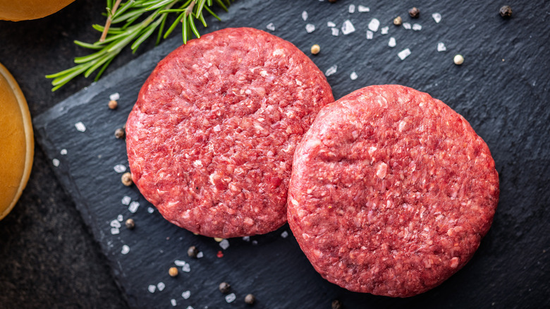 Raw burger patties on a black cutting board