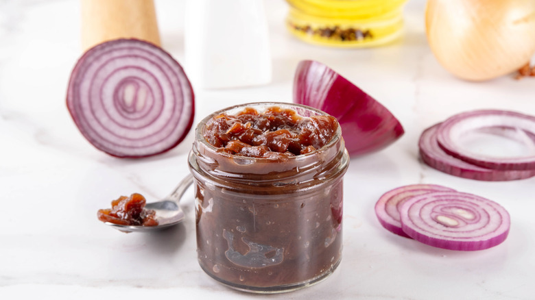 Red onion marmalade in a mason jar surrounded by slices of raw red onion