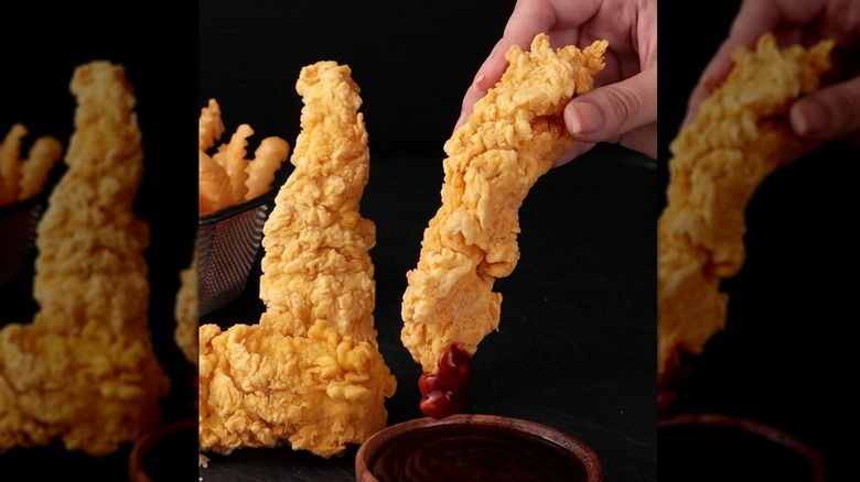 Closeup a hand dipping a piece of Church's chicken tenders into a sauce