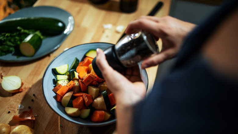 Adding pepper to bowl of vegetables for roasting