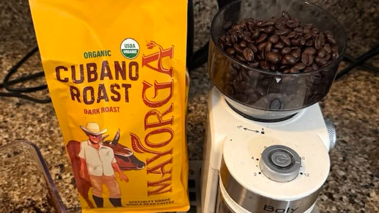Bag of Mayorga Café Cubano Roast and dark roast coffee beans in a grinder