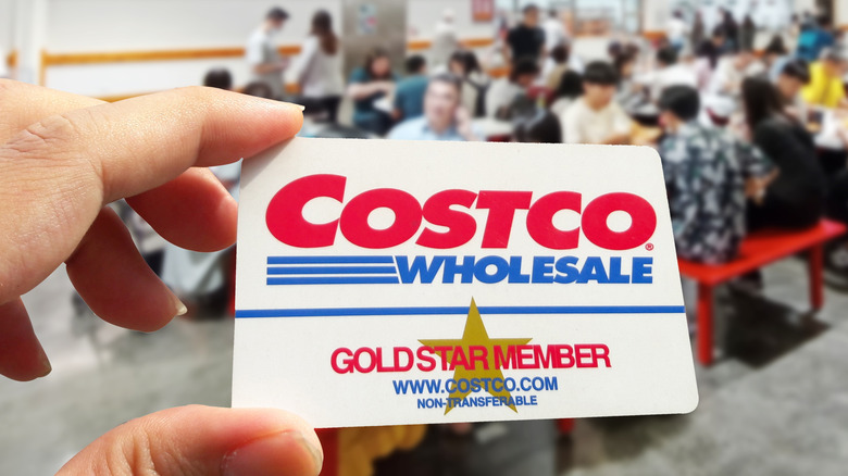 Hand holding Costco membership card in front of food court.