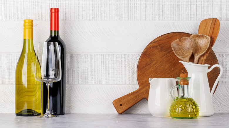 Bottles of wine on kitchen counter next to jugs and utensils
