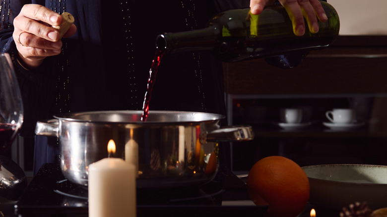 Body and hands of person shown pouring red wine into pan