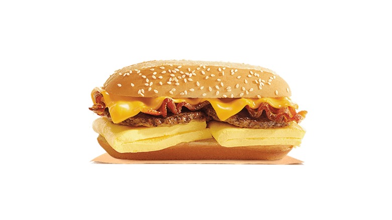Burger King breakfast sandwich with omelet-style eggs, two sausage patties, bacon, and American cheese on a sesame seed sub roll.