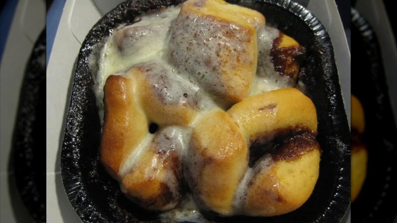 Close-up photo of McDonald's Cinnamelts topped with icing, in black disposable container.
