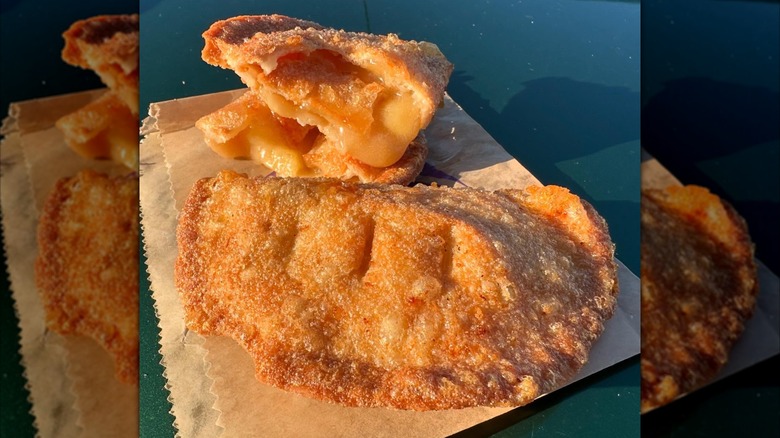 Two caramel apple empanadas on top of brown paper packaging, one cut in half displaying oozing filling.