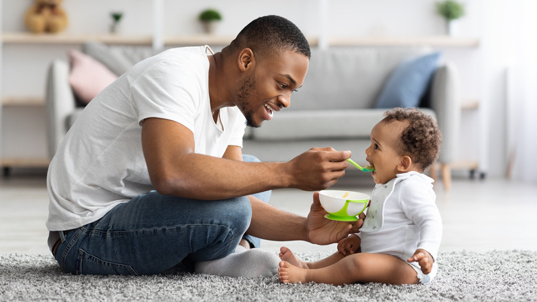 man feeding baby sat on carpet