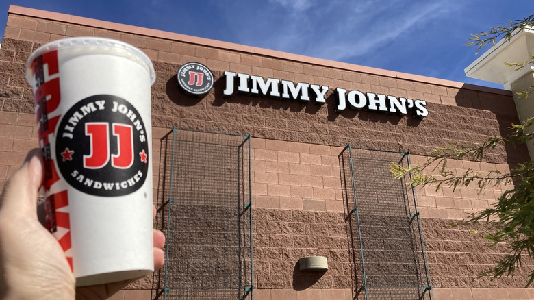 Hand holding up a Jimmy John's Coke outside the restaurant