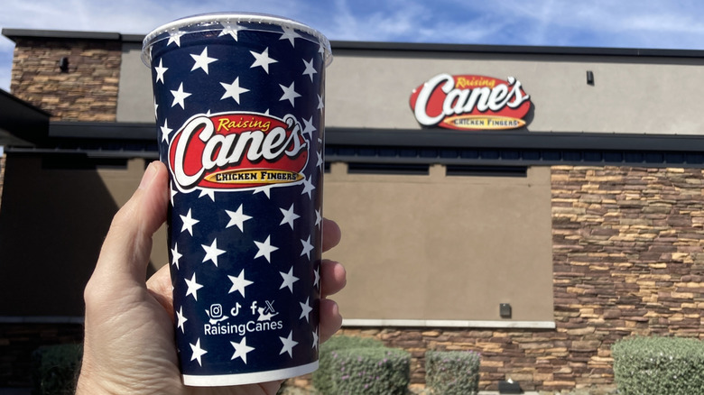 Hand holding a Raising Cane's Coke cup outside the restaurant