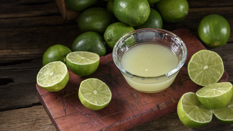 Glass bowl of lime juice surrounded by halved fresh limes