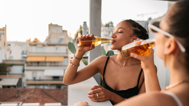 Two women drinking bottles of beer on balcony