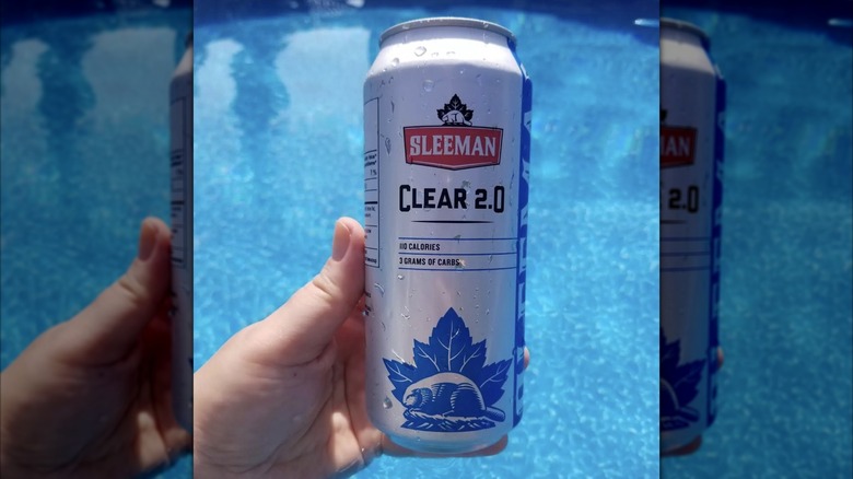 Hand holding can of Sleeman Clear with pool as backdrop