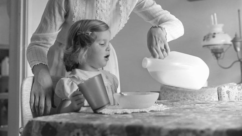 A woman pouring milk on a child's cereal