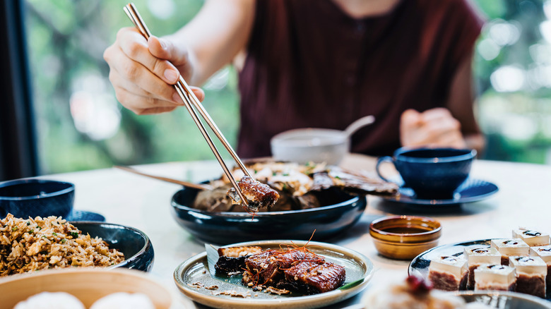 A person picking up food from dish on table with chopsticks
