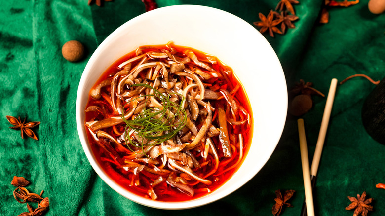 A white bowl containing Chinese food, red with hot peppers