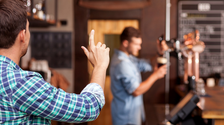 person at bar raising hand for attention