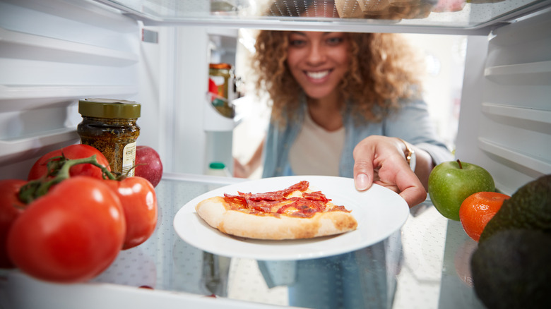 woman POV with pizza on plate in fridge