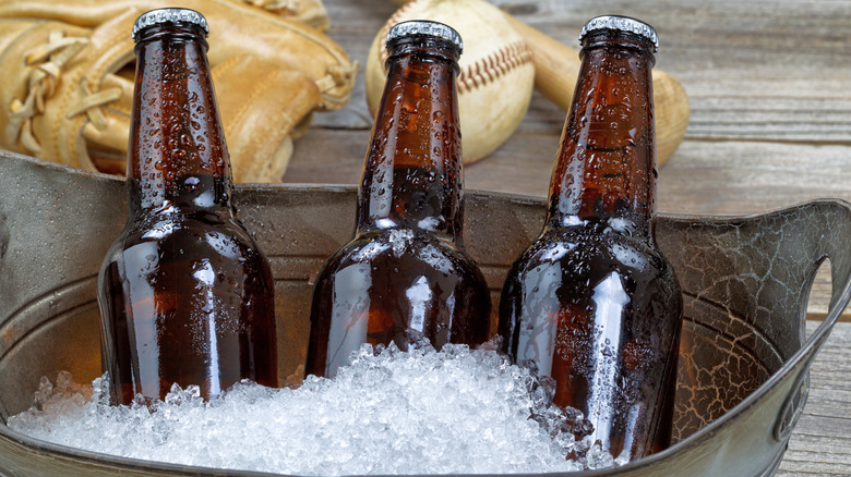 Three bottles of beer in ice bucket with baseball equipment in background