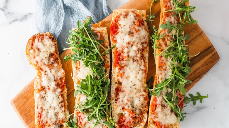French bread pizzas topped with arugula on a cutting board