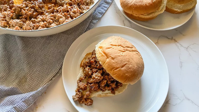 Sloppy Joes on a plate with dishes of ground meat and rolls in the background