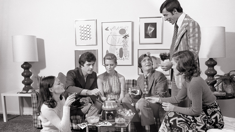 Six people in the 1970s enjoy fondue in the living room