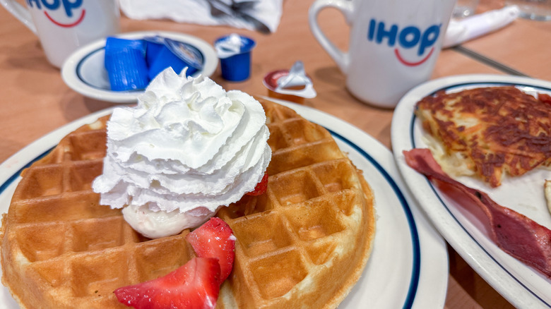 IHOP waffles on a white plate with a blue rim topped with shipped cream and fresh strawberries