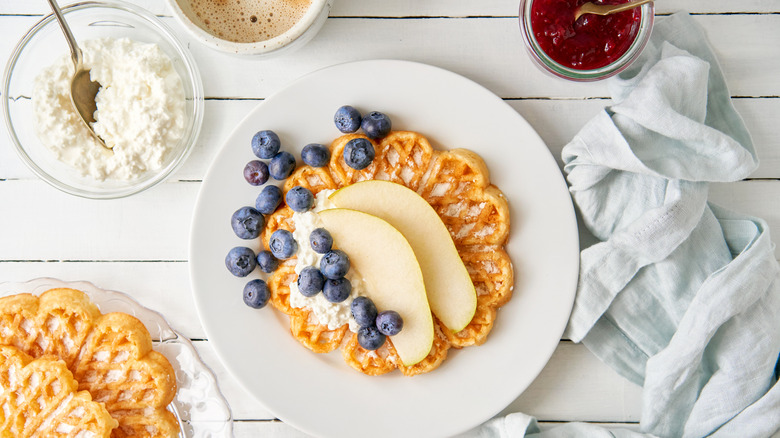 A bowl of cottage cheese next to a plate of waffles with apple slices and blueberries