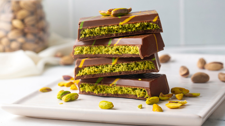 Stacked pieces of a Dubai chocolate surrounded by pistachio nuts on a white plate
