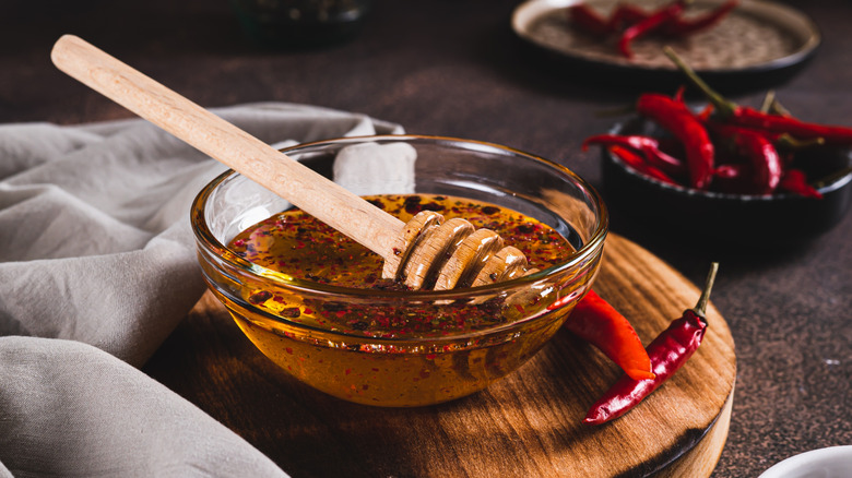 Red peppers next to a glass bowl of hot honey with a wooden honey stick resting in it
