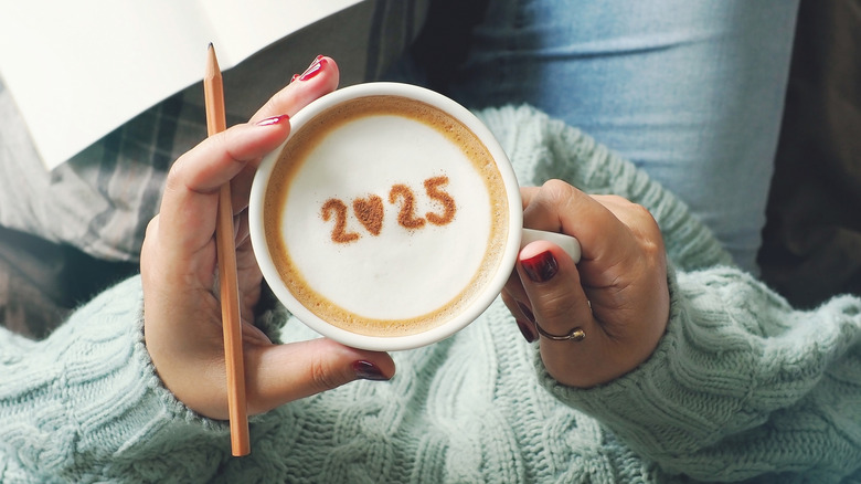 Someone holding a coffee with 2025 written in cocoa powder and foam on top