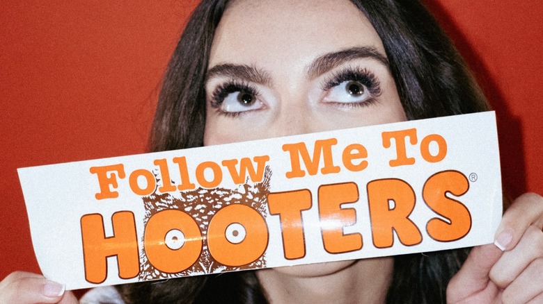 Woman holding Hooters sign in front of her face