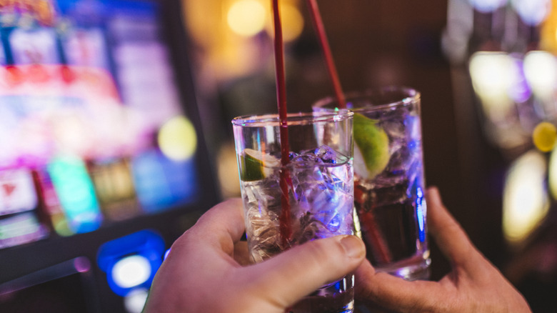 Two hands clinking cocktails in front of a slot machine