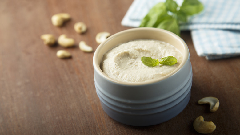 Cashew cream in a white crock on a wooden surface garnished with fresh herbs