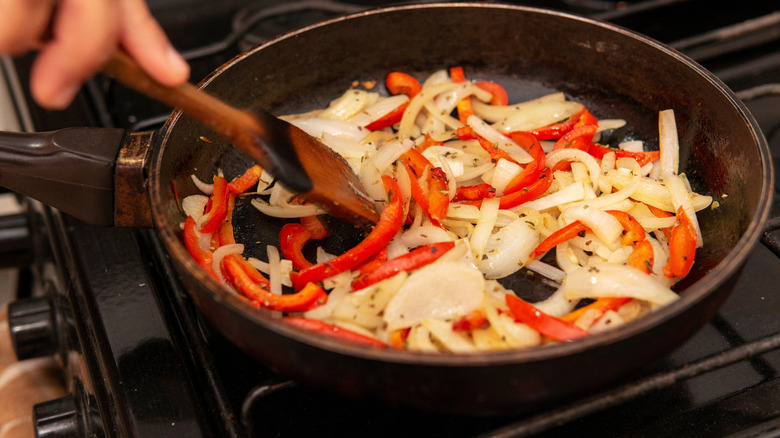 Onions and red bell peppers sautéing in a skillet